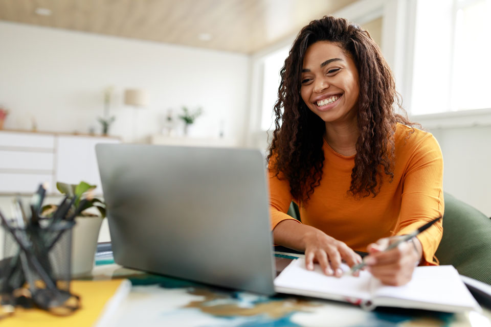 A smiling early learning professional takes notes while completing an online training session through the Professional Development Registry.